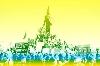 A protest crowd gather in front of a statue in Tijuana