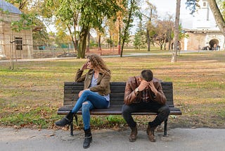 Couple sitting on a bench at a park, frustrated and not taking to each other.