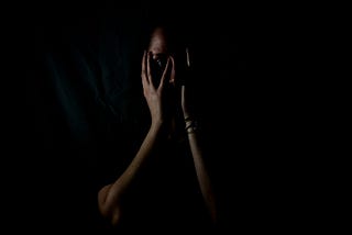 Women in the dark with hands covering face in fear