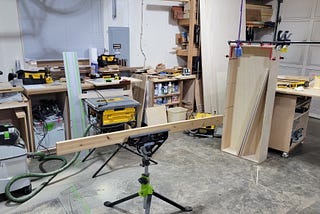 An overall view of the woodshop — a single garage bay with a lot of tools on all the surfaces and props and supports to facilitate working with larger pieces of wood despite not having big tools.