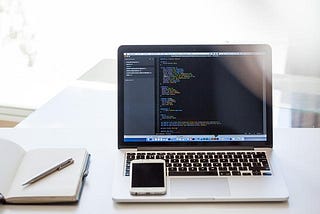 Photo of a laptop, phone, and notebook with a pen