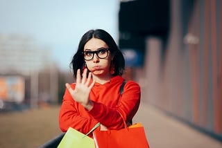 Woman holding shopping bags makes stop sign with her hand.