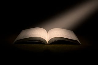 A shaft of light falls on the open pages of a book against a black background.