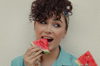 A woman putting a piece of watermelon in her mouth.