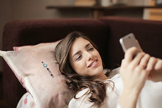 Woman in White Top Holding Smartphone Lying on Couch