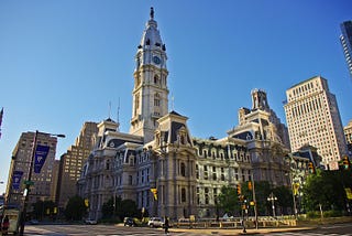 View of Philadelphia City Hall in central Philadelphia with buildings beside it, and blue skies behind it