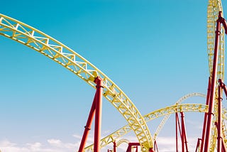 A close-up of red and yellow roller coaster against a blue sky