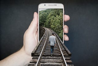 Man on a train track that runs into a phone held by a hand