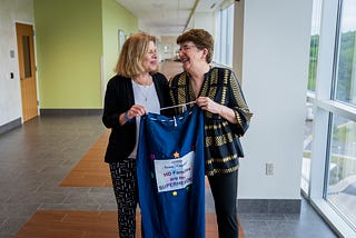 Genetic counselor smiles and looks at her nominator, holding a Huntington’s Disease banner