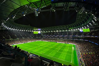 A football stadium filled with fans in the stands, with players playing on the pitch.
