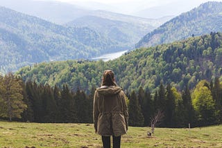 A woman contemplates a mountain landscape.