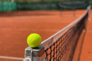 Tennis ball on tennis court balanced on post.