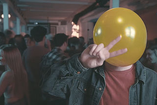 Still image from the short film Air Head showing a man at a party with a yellow balloon for a head.