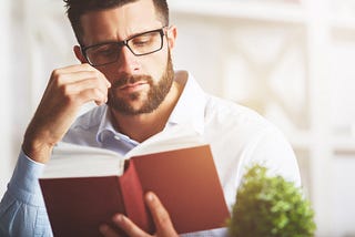 A man with a sad expression reading a red book.