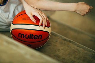 Close up of a woman’s hand and arm resting on a basketball.