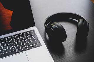 An open MacBook and a pair of wireless headphones rest on a work desk.