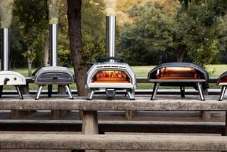 A lineup of several Ooni pizza ovens with the Fyra 12 on the far left, and the Ooni Karu 16 in the middle.