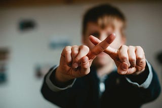 Young boy crossing his index fingers to form an “X”