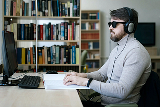 Blind web developer in front of the computer reading braille book