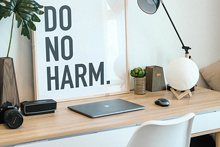 A desk with a laptop and a “Do no harm” sign.