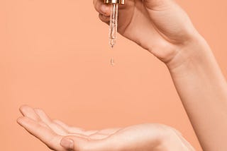 A drop of serum with glycolic acid falls into an open hand.
