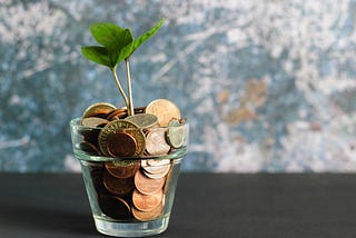 A glass filled with coins with a plant growing from it.