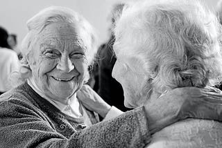Two elderly women embracing themselves happily