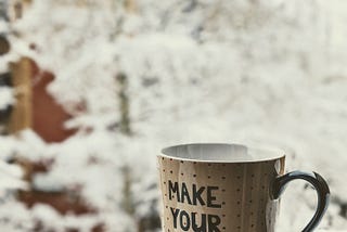 A mug with the words ‘Make your own magic’ sits on a bed of snow. Photo by Daniel D’Agostino