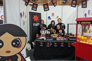 5 women standing behind a table in a NAB-branded booth