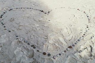 Pebbles forming large heart on sand with lots of footprints