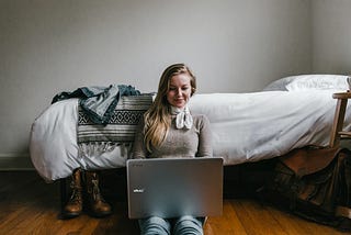 girl on laptop in front of bed