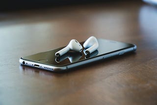 A pair of Apple air pods and an iPhone sitting on a table happily paired together