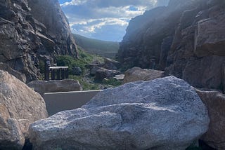 A mountain pass with partly cloudy blue skies is blocked by large boulders.