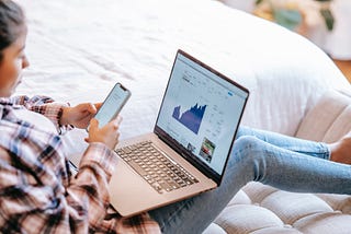 Woman with computer and phone with stocks on screen