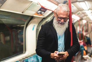 Older hipster man looks at phone on subway