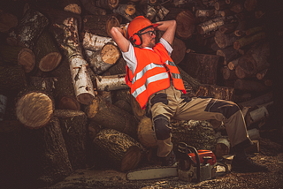 Man leaning back on logs of wood he cut.