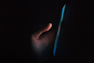 A hand holding a smartphone, with the screen illuminated in the dark