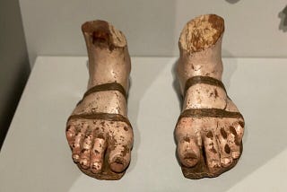 A sculpture of two dirty feet wearing roman sandals.
