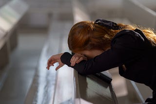 Woman in black mourning dress, head bowed into folded arms, grieving.