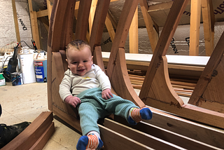 A baby boy lying smiling among stacked frames of a boat hull