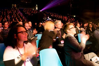 An audience of Interaction Awards attendees applaud. They are seated in a theatre and looking at the stage which is out of frame to the right.