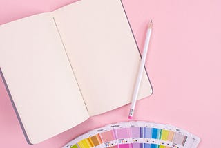 Photo of a notebook and printed Pantone colour cards sitting on a pink surface