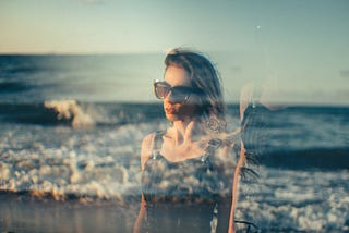 Woman standing in front of waves on beach, she is transparent as if fading away