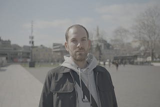 A man with hair loss standing outdoors in Istanbul, looking directly at the camera.