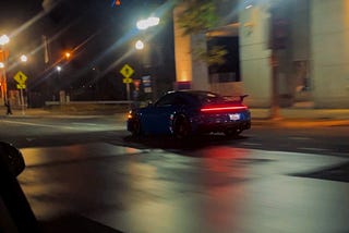 a midnight blue sports car (Porsche maybe) speeding down the empty city streets, after midnight.
