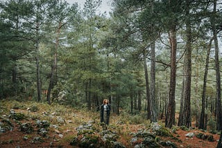 Woman standing in the forest, looking contemplative.