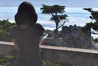 Me, standing by the ocean, looking out at the water and the Lone Cypress in Pebble Beach, California on a quiet, sunny day.