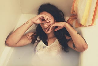 Crying woman, fully dressed woman laying in a bathtub filled with milky water.