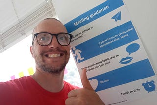 Gavin doing a thumbs up in front of the Meeting Guidance poster on the wall of a Cogapp meeting room