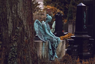 Statue of angel sitting on a bench in a cemetery